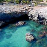 Torniamo cos� indietro e risaliamo la parete per affacciarci sulla costa rocciosa. Da qui su possiamo vedere la bocca della cavit�, che sbuca direttamente nel mare trasparente (foto di Pippo Vacca)